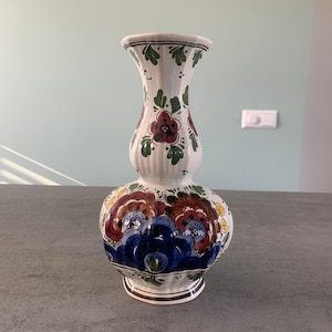 以下が含まれることがあります： 白磁の壺で、丸みのある胴体と細い首を持つ。壺は青、赤、黄、緑の色合いのカラフルな花柄で飾られている。