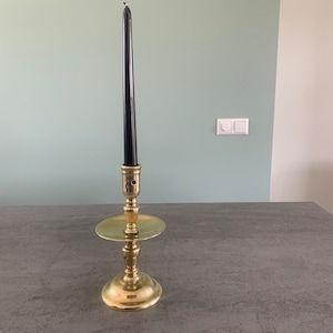 Puede incluir: Un candelero dorado con una vela negra sobre una superficie gris.