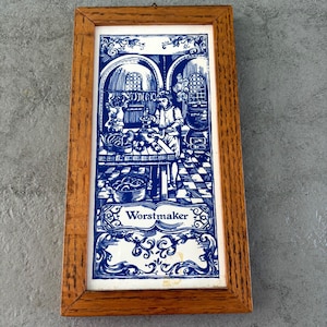 Puede incluir: Un azulejo azul y blanco enmarcado con la representación de una persona haciendo salchichas en una cocina. El azulejo tiene la palabra "Worstmaker" escrita en él.