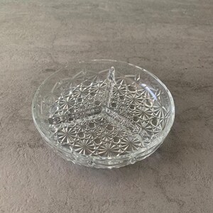 Op de afbeelding: Een glazen serveerschaal met drie compartimenten en een decoratief, geometrisch patroon.