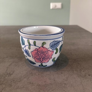 Peut inclure: Un petit pot en céramique blanche avec un bord bleu et un motif floral. Le motif présente des fleurs et des feuilles roses, bleues et vertes.