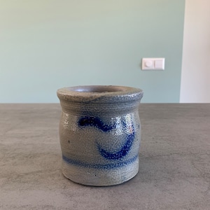 Op de afbeelding: Een grijze keramische pot met een blauw-wit ontwerp. De pot heeft een ronde vorm en een brede opening.