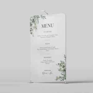 May include: A white wedding menu sign with a floral design. The menu includes starter, main, and dessert options. The sign has the word "MENU" at the top and is decorated with green leaves.