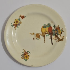 Puede incluir: Plato de cer&aacute;mica color crema con un dise&ntilde;o pintado de dos p&aacute;jaros posados en una rama con flores. Los p&aacute;jaros son amarillos, naranjas y verdes. Acentos florales en amarillo, naranja y azul.