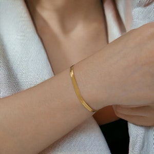 Peut inclure: Un bracelet fin en chaîne serpent de couleur or. Le bracelet est porté au poignet.