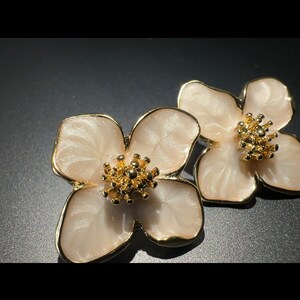 Peut inclure: Une paire de boucles d'oreilles en forme de fleur blanche avec des accents dorés. Les boucles d'oreilles ont un design délicat et féminin.