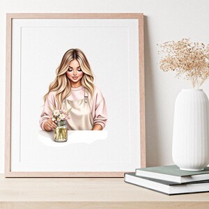 May include: A framed art print featuring a woman with long blonde hair, wearing a pink sweater and a light pink apron. She is holding a mason jar filled with flowers. A white vase with dried flowers sits nearby.