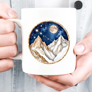 Pode incluir: Caneca de cer&acirc;mica branca com um design circular que retrata uma cordilheira sob um c&eacute;u estrelado e uma lua cheia. O design tem detalhes dourados e um fundo azul escuro. A caneca tem uma al&ccedil;a branca.