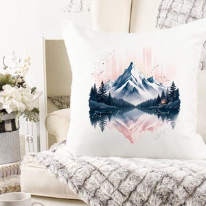 Pode incluir: Almofada quadrada branca com uma paisagem de montanha em aquarela com um lago e &aacute;rvores. O design inclui uma cordilheira em tons de azul e rosa, com um reflexo espelhado na &aacute;gua.