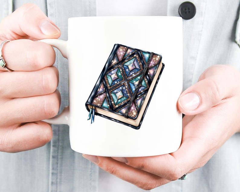 May include: White ceramic mug featuring a detailed illustration of a closed journal. The journal has a dark cover with a geometric design in shades of blue, teal, and purple, with glitter accents. A blue ribbon bookmark is visible.
