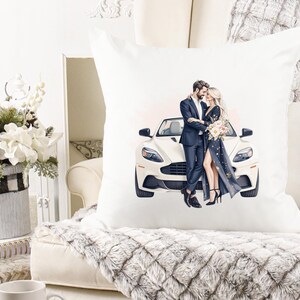 May include: Square white cushion with an illustration of a couple and a white sports car. The man is in a dark suit, and the woman wears a long, dark dress. The cushion is on a cream-coloured sofa with a faux fur throw.