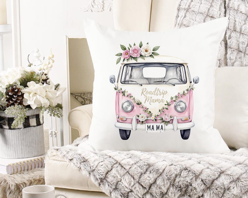 K&ouml;nnte beinhalten: Quadratisches wei&szlig;es Kissen mit einer rosa-wei&szlig;en Vintage-Van-Illustration. Der Van ist mit floralen Akzenten und dem Text "Roadtrip Mama" verziert. Das Nummernschild lautet "MAMA".