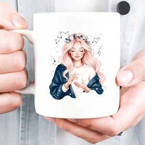 Pode incluir: Caneca de cer&acirc;mica branca com uma ilustra&ccedil;&atilde;o em aquarela de uma mulher com cabelo comprido e rosa e uma coroa de flores. A mulher usa uma camisa branca e um casaco azul escuro com desenhos de constela&ccedil;&otilde;es. A caneca tem uma al&ccedil;a branca.