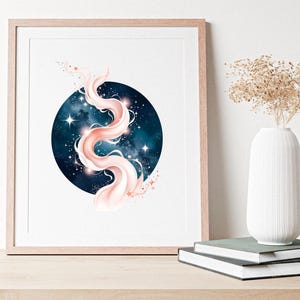 Pode incluir: Impress&atilde;o de arte emoldurada com um design celestial. Uma forma rodopiante, rosa claro e branca, &eacute; definida contra um c&iacute;rculo azul escuro cheio de estrelas. A obra de arte &eacute; exibida em uma superf&iacute;cie de madeira, com um vaso branco e livros.
