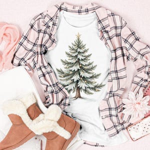 Puede incluir: Una camiseta blanca con un dise&ntilde;o de &aacute;rbol de Navidad en acuarela, combinada con una camisa a cuadros rosa, botas marrones con ribete de piel sint&eacute;tica y una bufanda rosa. Un cuaderno rosa, un tel&eacute;fono y una flor completan el conjunto festivo.