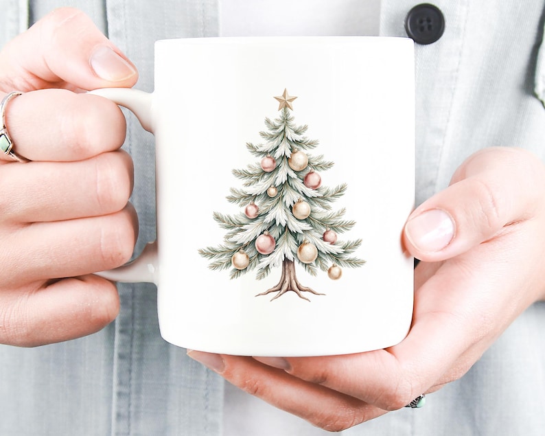 Puede incluir: Taza de cer&aacute;mica blanca con una ilustraci&oacute;n de acuarela de un &aacute;rbol de Navidad adornado con adornos rosas y dorados y una estrella dorada. El &aacute;rbol tiene agujas verdes y un tronco marr&oacute;n. La taza est&aacute; sostenida por una persona.