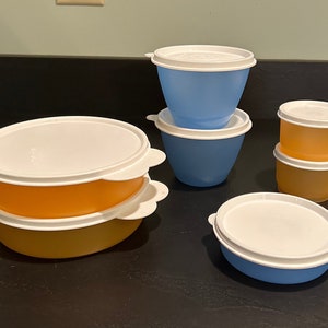 May include: A collection of plastic food storage containers in various sizes and colors. The containers are in shades of blue and orange, with white lids. Some containers are stacked, and all have a rounded shape.