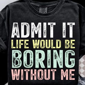 May include: Black t-shirt with the text "ADMIT IT LIFE WOULD BE BORING WITHOUT ME" in white, yellow, light green, and pink lettering. The shirt has a crew neck and a slightly faded appearance.