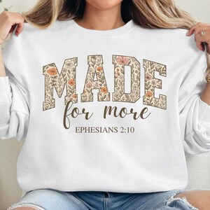 Op de afbeelding: Wit sweatshirt met een bloemenontwerp met de tekst "MADE for more EPHESIANS 2:10".