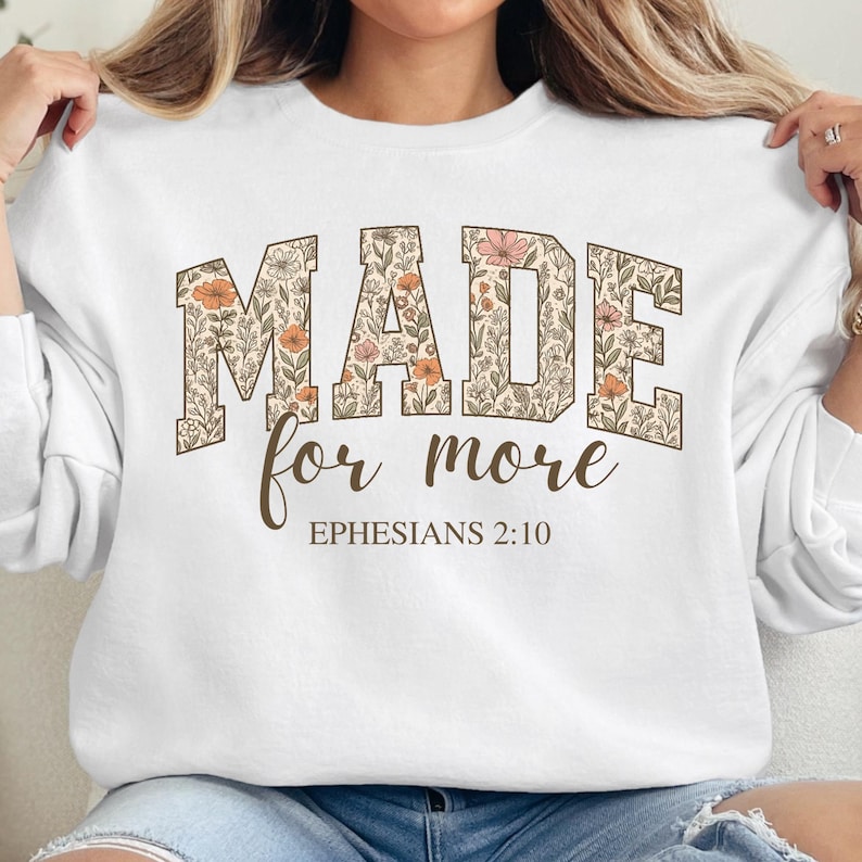 Op de afbeelding: Wit sweatshirt met een bloemenontwerp met de tekst "MADE for more EPHESIANS 2:10".
