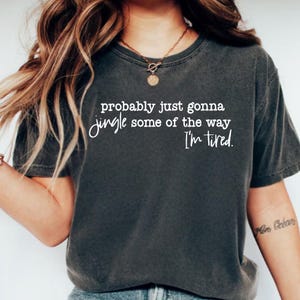 May include: Dark gray t-shirt with the text "probably just gonna jingle some of the way I'm tired" in white script. The shirt has a crew neck and short sleeves. The fabric appears soft and worn.