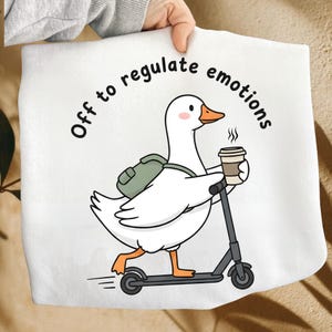 May include: A white ceramic mug with a black handle and the text "But First, Coffee" in a handwritten style. The mug is on a white surface. The mug is approximately 4 inches tall.