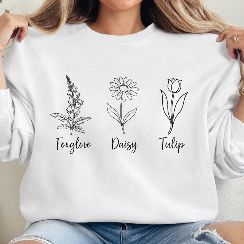 May include: White sweatshirt with a black line drawing of a foxglove, daisy, and tulip. The flowers are labeled "Foxglove", "Daisy", and "Tulip".