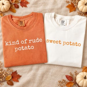 Puede incluir: Dos camisetas de manga corta y cuello redondo. La camiseta de la izquierda es de color naranja quemado con el texto blanco kind of rude potato. La de la derecha es blanca con el texto naranja sweet potato. Ambas tienen la etiqueta Comfort Colors.