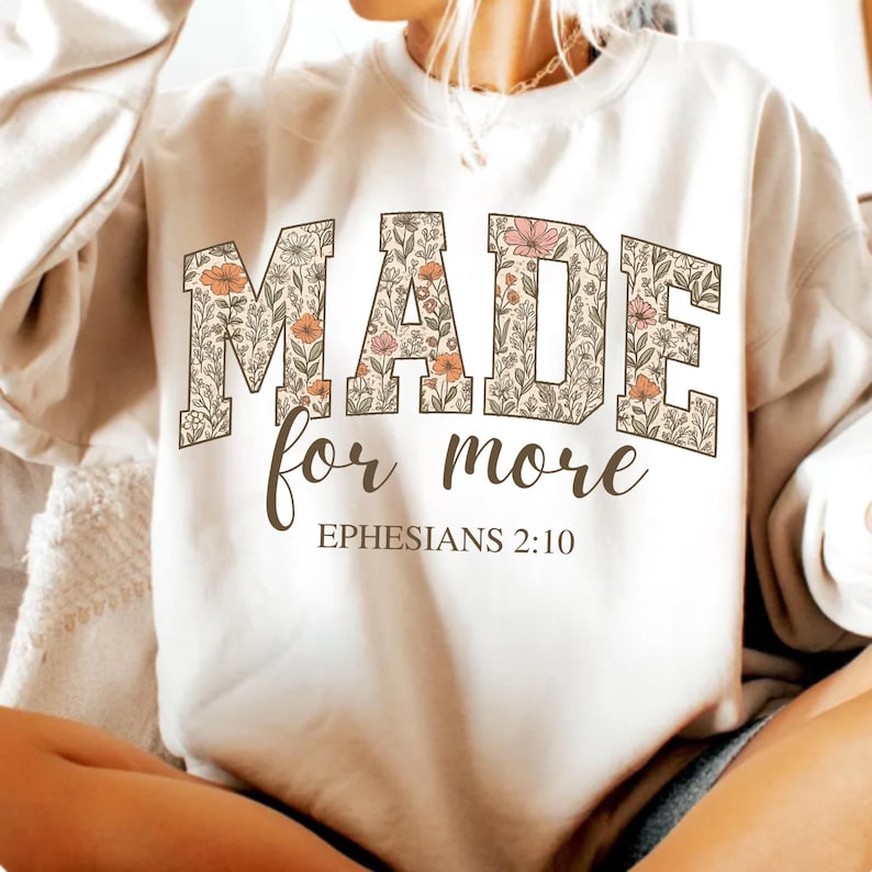 Op de afbeelding: Wit sweatshirt met een bloemenprint met de tekst "MADE for more EPHESIANS 2:10".