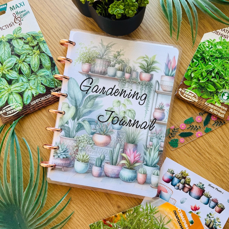 May include: A gardening journal with a watercolor illustration of potted plants on the cover. The journal has a gold spiral binding and the words "Gardening Journal" are printed in black on the cover.