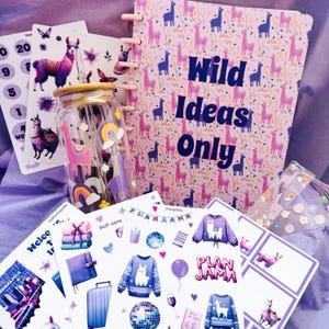 Op de afbeelding: Een roze en paarse planner met de tekst "Wild Ideas Only" op de kaft. De planner is omringd door verschillende stickers met lama's, regenbogen en andere ontwerpen. Er is ook een glazen waterfles met een bamboe deksel en een rietje.