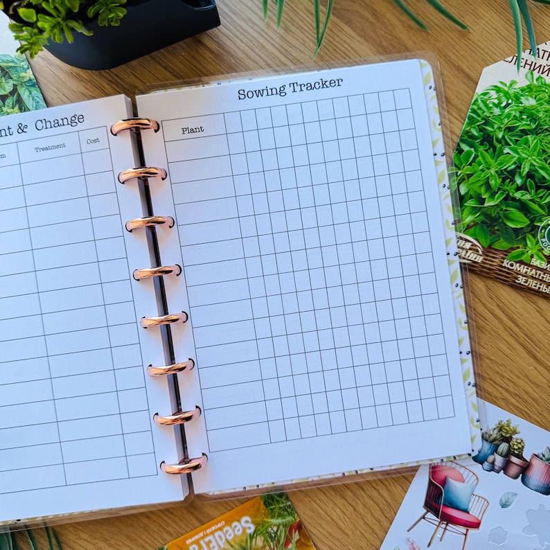 May include: A white planner with a gridded page for tracking sowing dates. The page is labeled "Sowing Tracker" and has a column for "Plant". The planner has a rose gold binding.