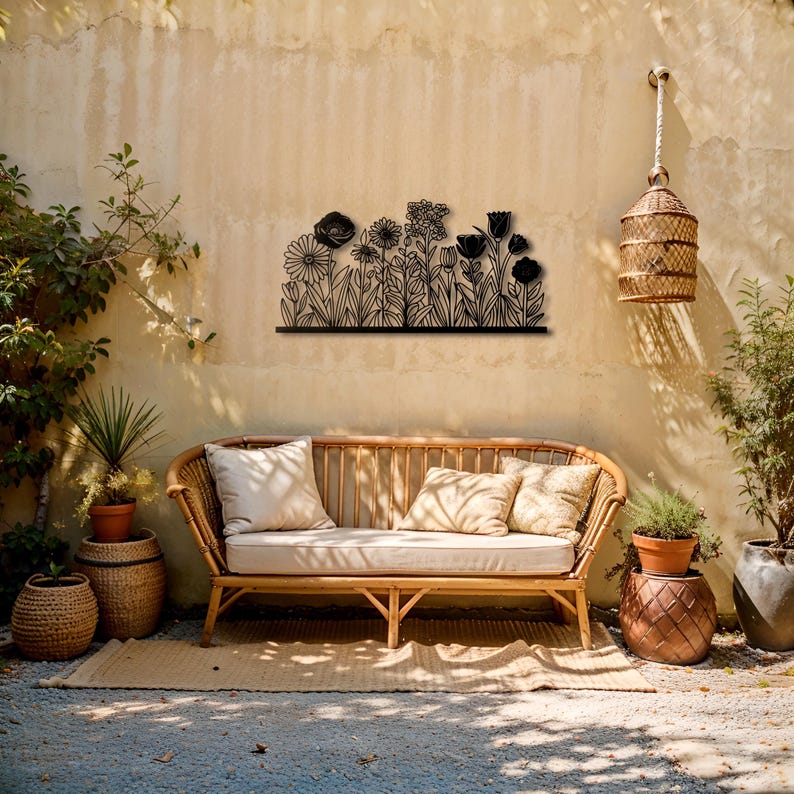 May include: Black metal floral wall art featuring various flower silhouettes. The artwork is mounted on a beige wall above a wicker sofa with cream-colored cushions. A woven birdcage hangs nearby, enhancing the outdoor aesthetic.