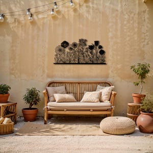May include: A black metal floral wall art piece is mounted on a beige wall above a wooden bench with cushions. The art features a silhouette of various flowers and foliage. The outdoor scene includes potted plants, a woven rug, and a string of lights.
