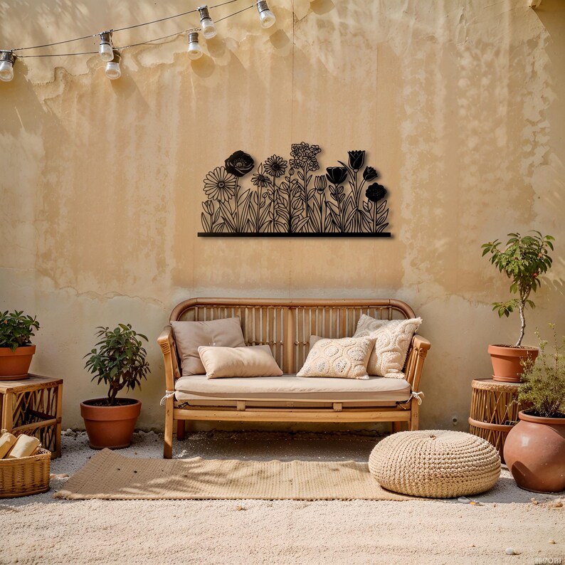 May include: A black metal floral wall art piece is mounted on a beige wall above a wooden bench with cushions. The art features a silhouette of various flowers and foliage. The outdoor scene includes potted plants, a woven rug, and a string of lights.