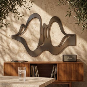 May include: A matte black metal wall art piece featuring an abstract, fluid, and organic shape with two large, interconnected open cutouts. The design consists of smooth, sweeping curves that create a continuous, flowing silhouette on the wall.
