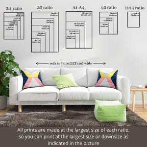 May include: A living room scene featuring a white sofa with colorful throw pillows and a green ottoman. Above the sofa, various framed print sizes are displayed, with measurements in inches and centimeters. Text indicates the sofa is 84 inches wide.