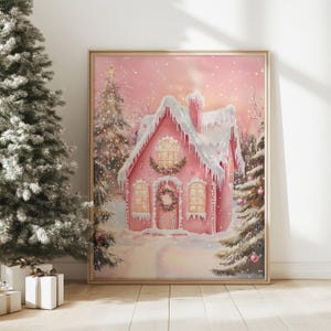 May include: A framed print of a pink gingerbread house covered in snow, surrounded by snow-covered evergreen trees. The house has a wreath on the door and a star on top. The artwork is set in a winter wonderland scene.