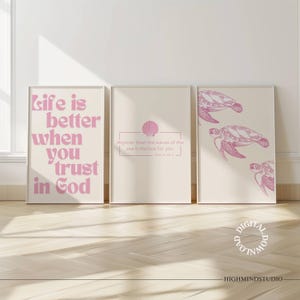 May include: Three framed art prints with a light beige background. The left print has the text "Life is better when you trust in God" in pink. The middle print has a pink seashell graphic and text. The right print features pink sea turtle illustrations.