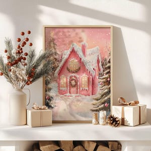 May include: A framed print of a pink gingerbread house covered in snow, with a wreath on the door and lights in the windows. The artwork is set in a snowy forest scene, with a vase of berries and a wrapped gift box in the foreground.