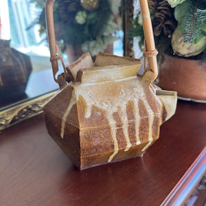 May include: A brown ceramic teapot with a geometric design and a bamboo handle. The teapot has a light-colored glaze that drips down the sides. The handle is woven at the top.
