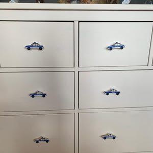 Könnte beinhalten: Weiße Kommode mit fünf Schubladen. Jede Schublade hat einen blauen und weißen Polizeiwagen-Zuggriff.