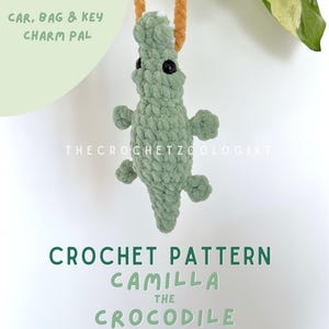 Può includere: Un ciondolo a forma di coccodrillo verde all'uncinetto, con occhi neri e piccoli arti, appeso a un cordino marrone. Il testo sull'immagine recita "CAR, BAG & KEY CHARM PAL" e "CROCHET PATTERN CAMILLA THE CROCODILE". The Crochet Zoologist è anche stampato.