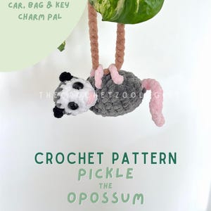 Op de afbeelding: Een gehaakte opossum-bedel met grijze, witte en roze details, hangend aan een bruin koord. De tekst "CAR, BAG & KEY CHARM PAL" en "CROCHET PATTERN PICKLE THE OPOSSUM" zijn ook zichtbaar.
