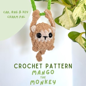 Pode incluir: Um amuleto de carro de macaco de crochê em tons de marrom e creme, pendurado por um cordão verde. O amuleto tem olhos pretos e uma pequena cauda. O texto na imagem diz: "CAR, BAG & KEY CHARM PAL" e "CROCHET PATTERN MANGO THE MONKEY".