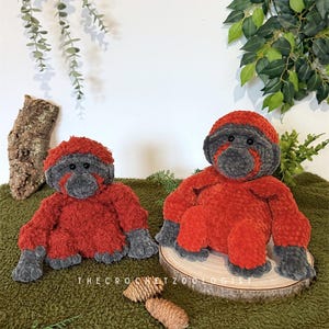 May include: Two handmade crochet orangutan plush toys. The plush toys are red with gray faces, hands, and feet. One plush toy sits on a wooden slice, and the other sits on a green surface. The text "THE CROCHET ZOOLOGIST" is visible.