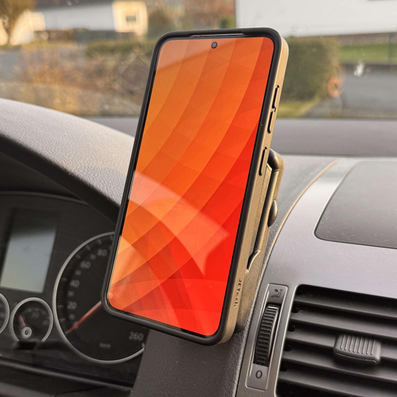 May include: A smartphone with an orange and red gradient screen is mounted in a car. The phone is in a black case and is held by a tan phone mount attached to the dashboard. The dashboard is gray.