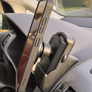 May include: Black smartphone in a protective case mounted on a car dashboard phone holder. The phone is angled, displaying the screen. The phone holder is black and has a rotating knob. The brand name "Jetech" is visible on the phone case.