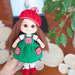 May include: A crocheted doll with brown hair, a red and white hat, and a green dress with white and red accents.