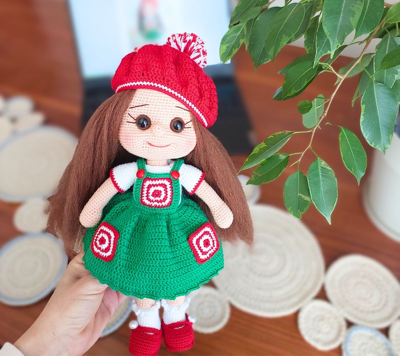 May include: A crocheted doll with brown hair, a red and white hat, and a green dress with white and red accents.